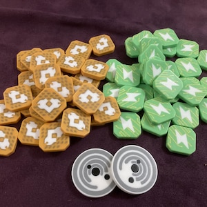 May include: A selection of game pieces, including tan square tiles with white designs, green square tiles with lightning bolt graphics, and two grey circular tokens with concentric patterns. The pieces are arranged on a purple surface.