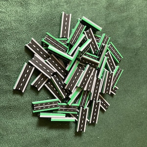 May include: A pile of black and green road pieces for a board game. The pieces are made of plastic and have a white line down the center.
