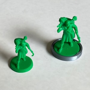 Op de afbeelding: Twee groene plastic figuurtjes van mensen die voorwerpen op hun rug dragen. De figuurtjes staan op groene bases. Het grotere figuurtje staat op een grijze basis.