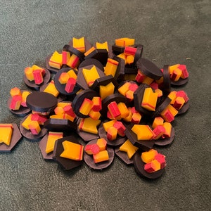 Puede incluir: Un montón de piezas de juego negras y amarillas con acentos rojos. Las piezas tienen forma de banderas, hexágonos y otras formas geométricas.
