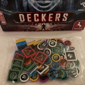 May include: A board game box titled "DECKERS" with a person silhouette. A clear bag contains game pieces in red, green, blue, yellow, and white. The game pieces are square, round, and rectangular.
