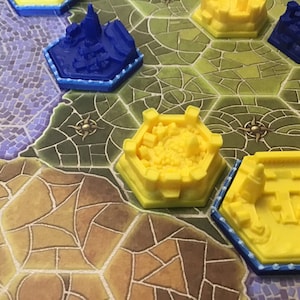 Puede incluir: Primer plano de un juego de mesa con piezas de plástico amarillas y azules. Las piezas tienen forma de castillos y ciudades. El tablero está hecho de un material verde y marrón.