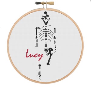 May include: A white embroidery hoop with a black skeleton design and the name "Lucy" in red lettering.