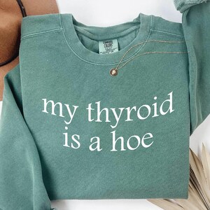 May include: Light green sweatshirt with the text "my thyroid is a hoe" printed in white.