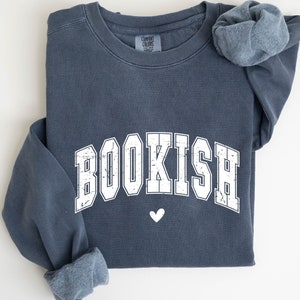May include: A dark blue sweatshirt with the word "BOOKISH" printed in white with a distressed look. The word is in a collegiate font with a small white heart below it.