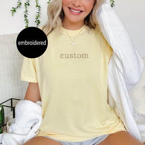 May include: A yellow t-shirt with the word "custom" embroidered on the front in a light brown thread.