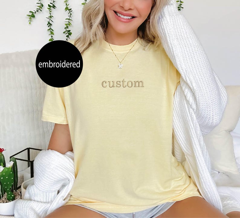 May include: A yellow t-shirt with the word "custom" embroidered on the front in a light brown thread.