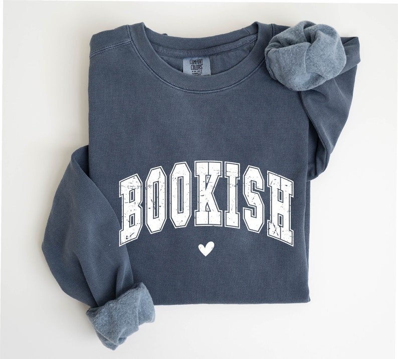 May include: A dark blue sweatshirt with the word "BOOKISH" printed in white with a distressed look. The word is in a collegiate font with a small white heart below it.