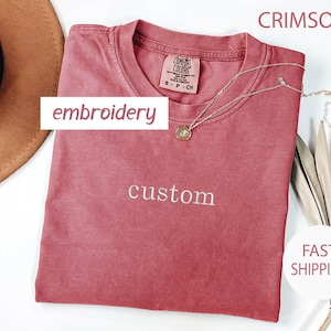 May include: Crimson red t-shirt with the word "custom" embroidered in white on the front. The shirt is made of a soft, comfortable material and has a relaxed fit.