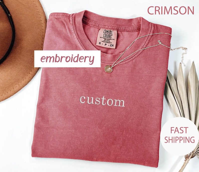 May include: Crimson red t-shirt with the word "custom" embroidered in white on the front. The shirt is made of a soft, comfortable material and has a relaxed fit.