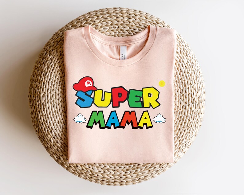 May include: A pink t-shirt with a graphic of a Super Mario character wearing a red cap and the text "Super Mama" in rainbow colors.