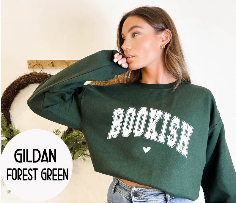 May include: A forest green Gildan sweatshirt with the word "BOOKISH" in white with a distressed look. A small white heart is below the word.