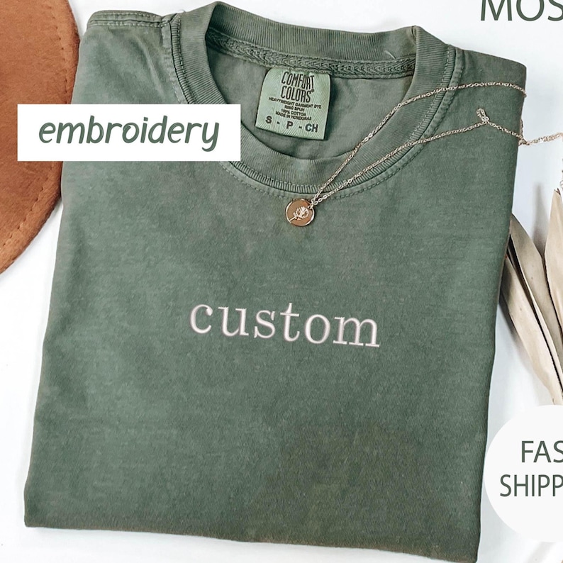 May include: A green t-shirt with the word "custom" embroidered on the front in white thread. The shirt is made of a soft, comfortable fabric and has a relaxed fit.
