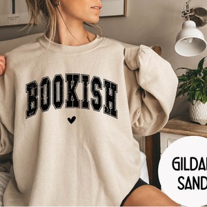 May include: A beige sweatshirt with the word "BOOKISH" printed in black with a small heart below it. The sweatshirt is made by Gildan and is in the color Sand.