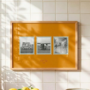Puede incluir: Un marco de madera rectangular que contiene un paspartú amarillo mostaza con tres fotos en blanco y negro estilo sello postal. Las fotos muestran una furgoneta, personas en una playa y palmeras. El texto "Road Trip 2023" está impreso en el centro.