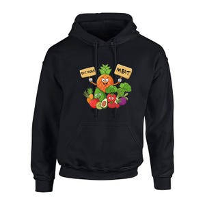 Op de afbeelding: Zwarte hoodie met een cartoon ananas karakter met borden met de tekst "EAT MORE" en "MEAT". De ananas is omringd door cartoon groenten zoals broccoli, avocado en tomaten. Het ontwerp is op de voorkant gedrukt.