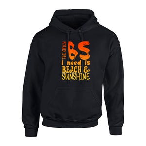Op de afbeelding: Zwarte hoodie met de tekst "THE ONLY BS I NEED IS BEACH & SUNSHINE" in oranje en geel. De hoodie heeft een capuchon met trekkoord en een voorzak.