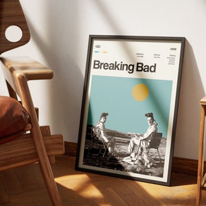 May include: A black framed poster with a minimalist design featuring two figures in hazmat suits sitting on chairs in a desert landscape. The poster has the title "Breaking Bad" in bold white text and the year "2008" in the top right corner.
