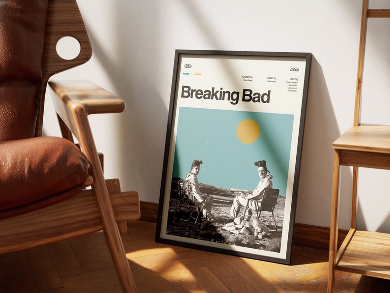 May include: A black framed poster with a minimalist design featuring two figures in hazmat suits sitting on chairs in a desert landscape. The poster has the title "Breaking Bad" in bold white text and the year "2008" in the top right corner.
