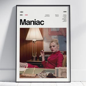 May include: A framed poster with the title "Maniac" in bold black letters. The poster features a woman in a red suit, seated at a desk. The poster includes the year 2018, and the names of the creator, music composer, and actors.