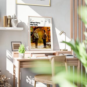 May include: A framed poster with the text "When Harry Met Sally" displayed on a wooden desk. The poster features a movie scene with two people. The desk also holds a small lamp, books, and a small plant.