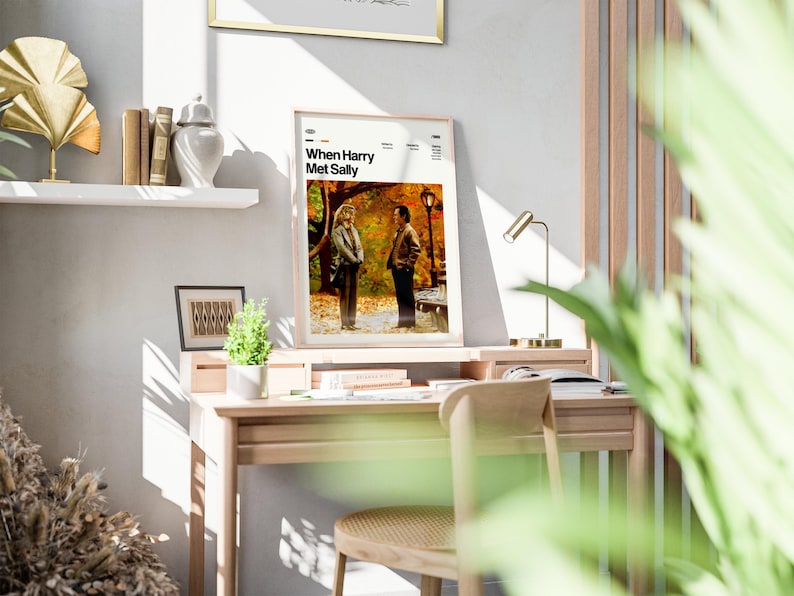 May include: A framed poster with the text "When Harry Met Sally" displayed on a wooden desk. The poster features a movie scene with two people. The desk also holds a small lamp, books, and a small plant.