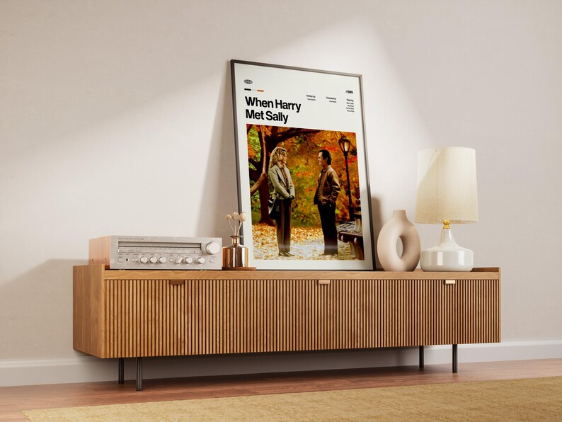 May include: A framed movie poster for "When Harry Met Sally" stands on a wooden cabinet. The cabinet has a ribbed design and holds a stereo, a vase, and a lamp. The poster features two people in a park setting.