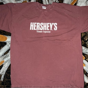 May include: A maroon t-shirt with a white graphic that says "HERSHEY'S Times Square".