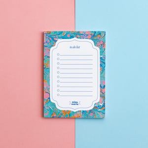 Pode incluir: Um bloco de notas marmoreado azul e rosa com uma seção de lista de tarefas brancas. O bloco de notas tem uma borda branca com um design decorativo e o texto "to do list" na parte superior. A parte inferior do bloco de notas tem o texto "mini maria" em uma caixa branca.