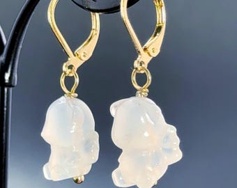 May include: A pair of gold-colored leverback earrings with white, translucent bear-shaped charms. The charms have a smooth, polished finish and are suspended from the gold-toned ear wires. The earrings are displayed against a dark background.