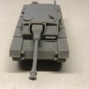 May include: A gray model tank with a long barrel and detailed features. The miniature tank has a rectangular body with visible tracks and a turret. The model is made of a solid, matte material.