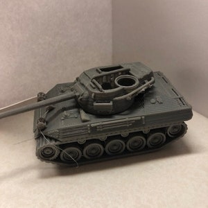 May include: A gray plastic model of a tank with a raised turret and a detailed design. The tank has a long barrel and a series of wheels on the underside.