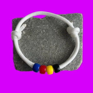 Peut inclure: Bracelet en paracorde blanc avec des perles bleues, rouges, jaunes et noires.