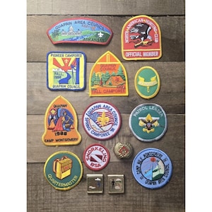 Puede incluir: Una colección de doce parches de exploradores bordados y dos pines de metal con diversas formas, colores y diseños, incluyendo textos como Quapaw Area Council, North American Hunting Club, Pioneer Camporee, Fall Camporee, Camp Montgomery y Patrol Leader.