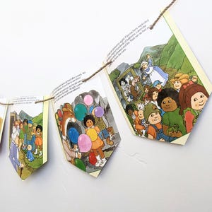 Könnte beinhalten: Eine Girlande aus illustrierten Bilderbuchseiten, die mit Bindfaden zusammengebunden sind. Die Illustrationen zeigen Kinder, Luftballons und eine Frau in einem blauen Kleid. Der Text auf den Seiten lautet "Firecrackers exploded and the Kids ran as fast as the mine."