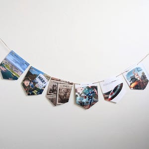 Puede incluir: Una hilera de banderines con varias im&aacute;genes, incluyendo un titular de peri&oacute;dico que dice "WAR!" y una imagen de c&oacute;mic de Capit&aacute;n Am&eacute;rica. Los banderines est&aacute;n colgados en una pared blanca.