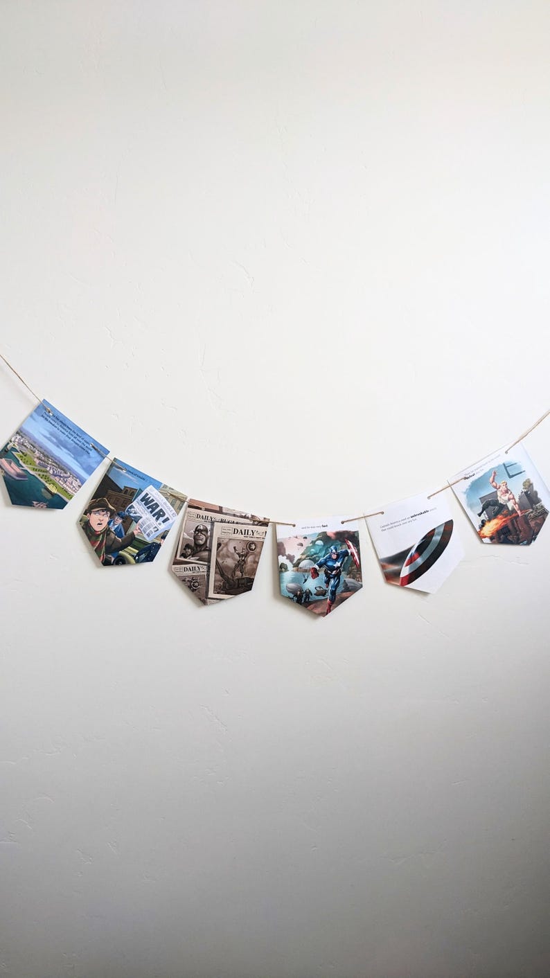 Puede incluir: Una hilera de banderines con varias im&aacute;genes, incluyendo un titular de peri&oacute;dico que dice "WAR!" y una imagen de c&oacute;mic de Capit&aacute;n Am&eacute;rica. Los banderines est&aacute;n colgados en una pared blanca.