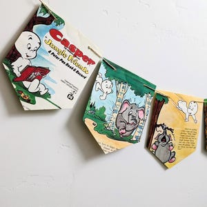 以下が含まれることがあります： ヴィンテージの子供向け絵本のページで作られたバナー。キャスパー・ザ・フレンドリー・ゴーストとジャングル・フレンズのイラストが特徴です。ペナントは紐でつながれており、象とキャスパーの漫画のシーンが描かれています。