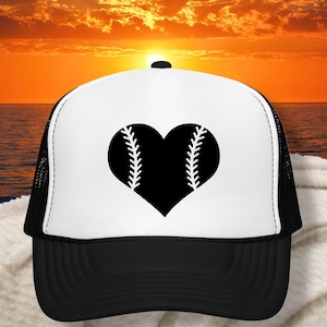 May include: A black and white baseball cap with a heart-shaped baseball design. The heart is black with white stitching, and the cap has a black brim and mesh back. The background shows a sunset over the ocean.