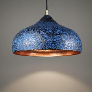 May include: A blue and copper pendant light fixture. The shade has a textured, crackled pattern in shades of blue and black. The interior of the shade is copper-colored, and the fixture hangs from a black cord.