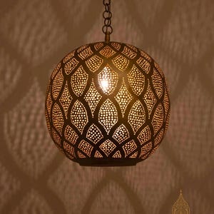 May include: A spherical, bronze-colored pendant light with intricate cut-out patterns. The light fixture hangs from a chain and casts decorative shadows. The brand name "NUBARI LIGHTS" is visible at the bottom.