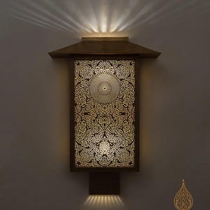 May include: A decorative wall sconce with an intricate, openwork design. The rectangular light fixture features a detailed floral pattern and a warm, golden glow. The sconce is mounted on a wall and emits light upwards and downwards.