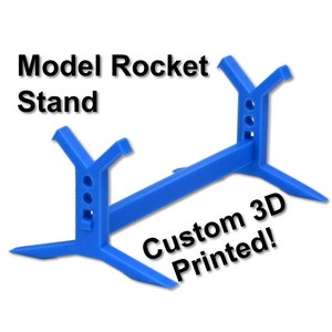 May include: A blue 3D printed model rocket stand. The stand has a base with three legs and a center bar to hold the rocket. The text "Custom 3D Printed!" is printed on the stand.