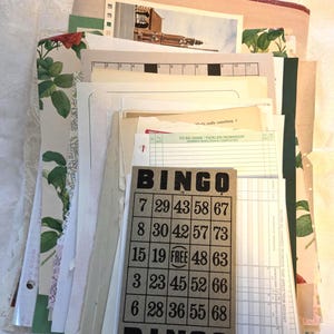 May include: A collection of vintage ephemera, including a bingo card, lined paper, and botanical print pages. The bingo card is gray with black numbers and the word "BINGO" at the top and bottom. Other papers include a photo and a "tickler reminder".