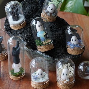 以下が含まれることがあります： コルク栓付きのミニチュアガラステラリウムのコレクション。それぞれにユニークな手作りのフィギュアが入っています。フィギュアには、幽霊、猫、その他の気まぐれなデザインがあり、花や苔などの装飾要素が使用されています。