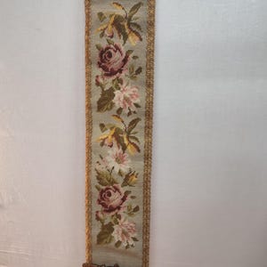 Könnte beinhalten: Ein antiker Wandbehang aus Nadelspitze mit einem floralen Muster. Der Behang hat einen goldenen Rand und einen Messinghaken unten.