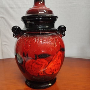 Può includere: Vaso in ceramica rossa con coperchio nero e un design nero e rosso di frutta. Il vaso ha la scritta "Ramtop" sul davanti.