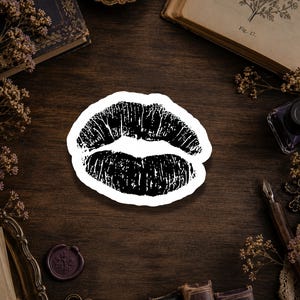 May include: A die-cut sticker featuring a black ink-style graphic of a pair of lips. The design displays a textured, stamped appearance with visible vertical lines across both the upper and lower lips, set against a clean white border.