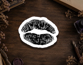 May include: A die-cut sticker featuring a black ink-style graphic of a pair of lips. The design displays a textured, stamped appearance with visible vertical lines across both the upper and lower lips, set against a clean white border.
