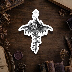 May include: A die-cut sticker featuring a black and white ink illustration of a sword centered in front of a mountain range. The sword is wrapped in a rose vine with thorns and features large, detailed bat-like wings extending from the hilt.
